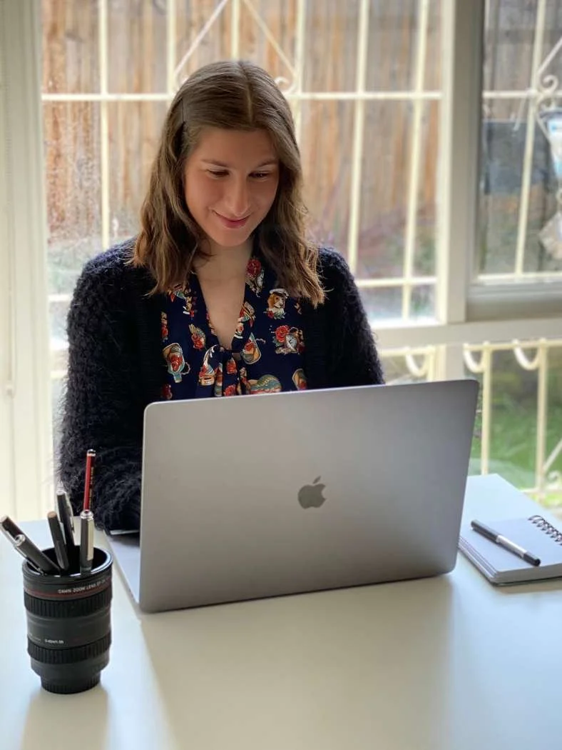 Sarah in the early stages of her freelance business sitting at a desk on her laptop with a notebook and pen. The office is bright and inviting.