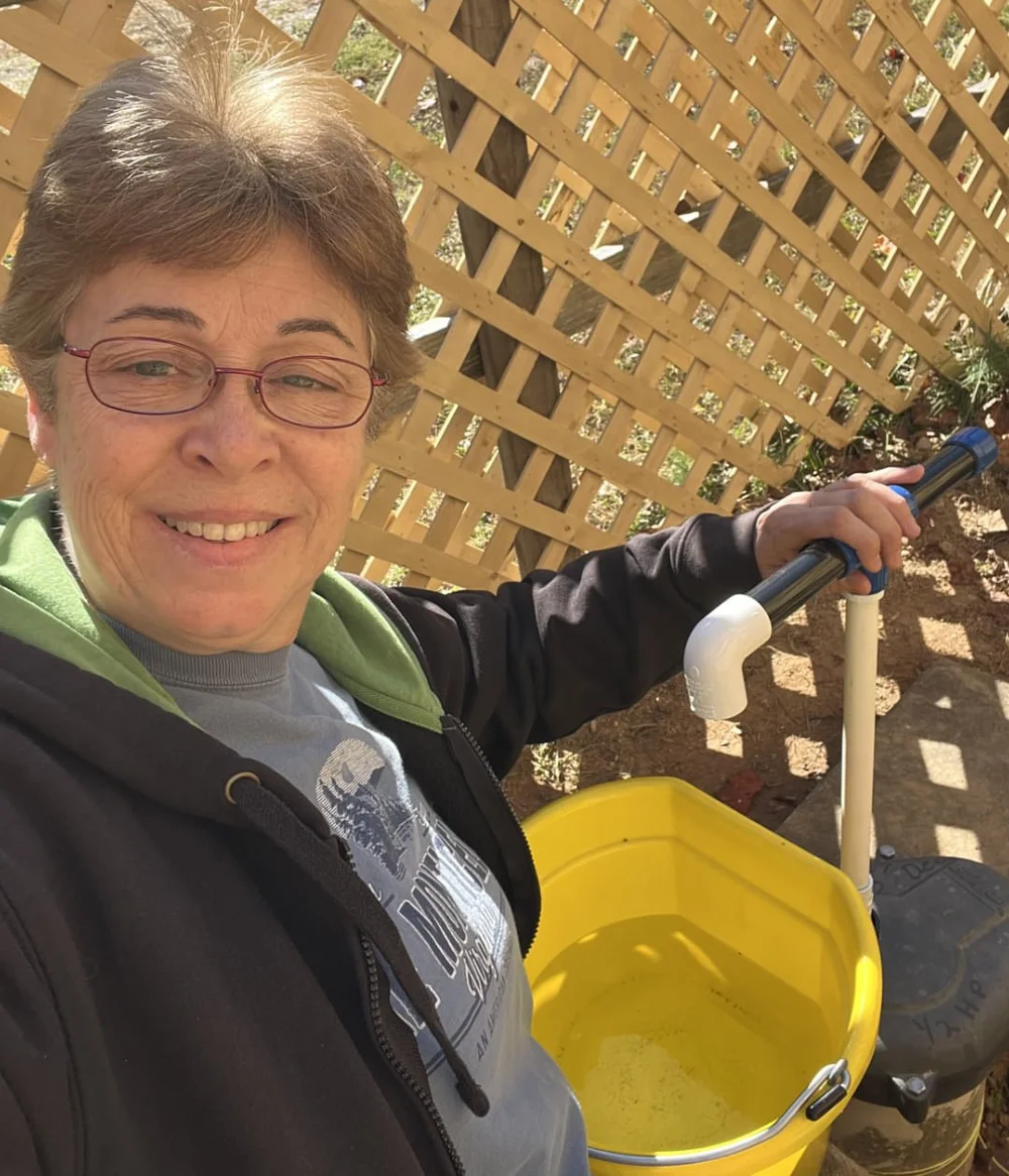 Barbara beside her installed hand pump and a yellow bucket of water