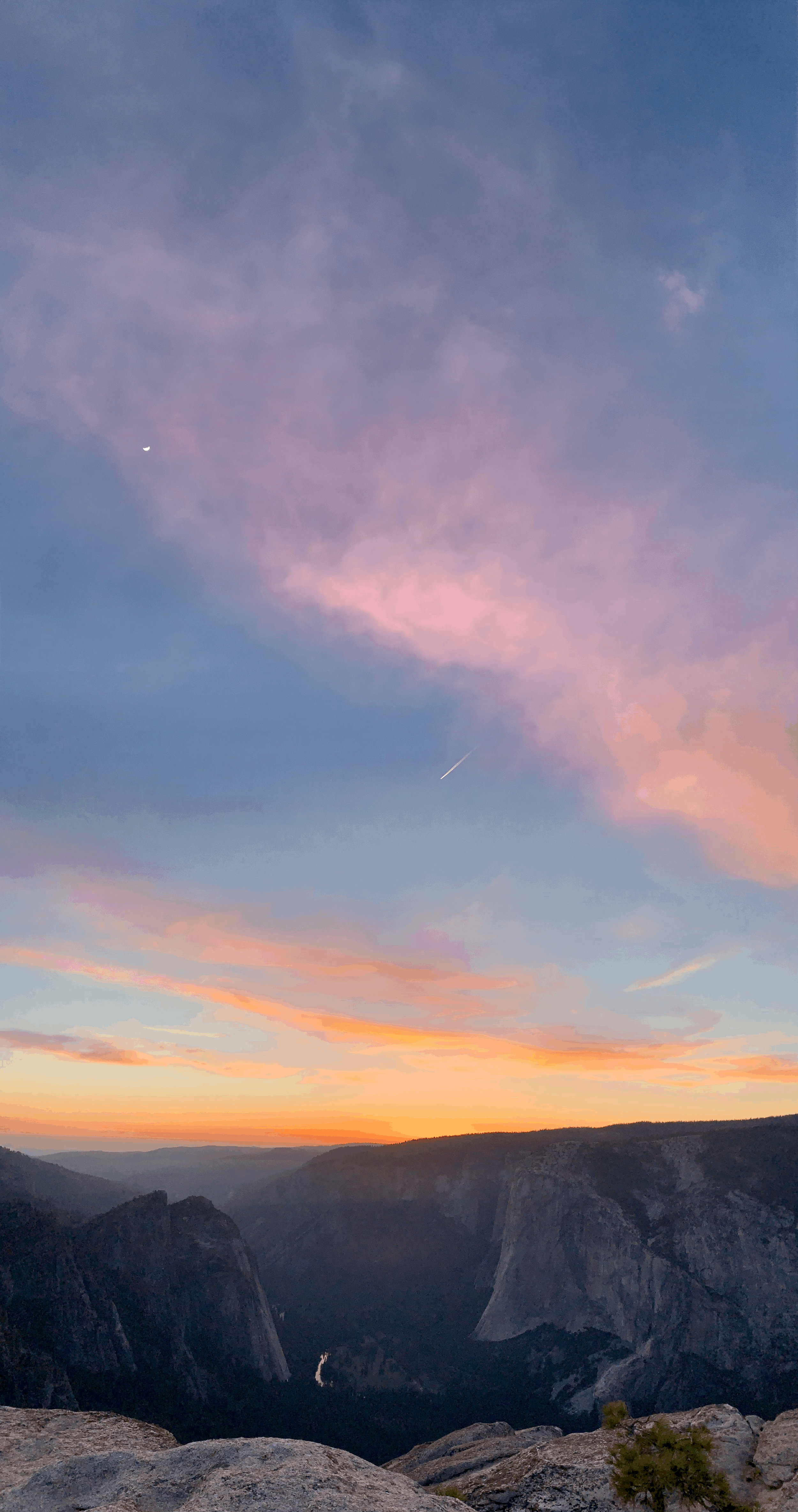 Sunset over a canyon with pink and orange clouds and a moon visible in the sky.