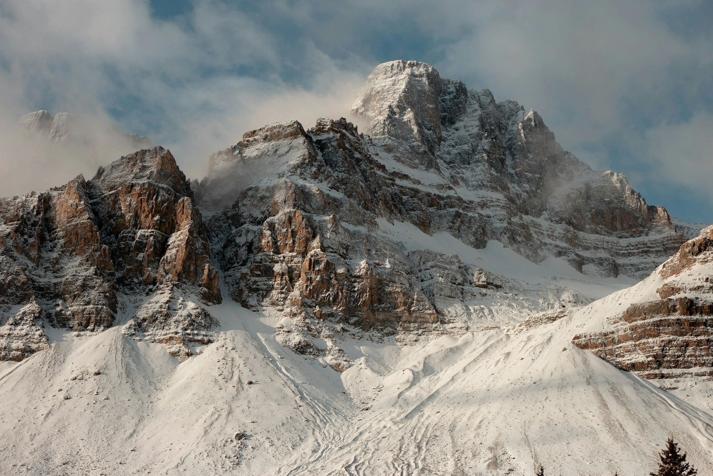 Snow-covered mountain range with a cloudy sky in the background.