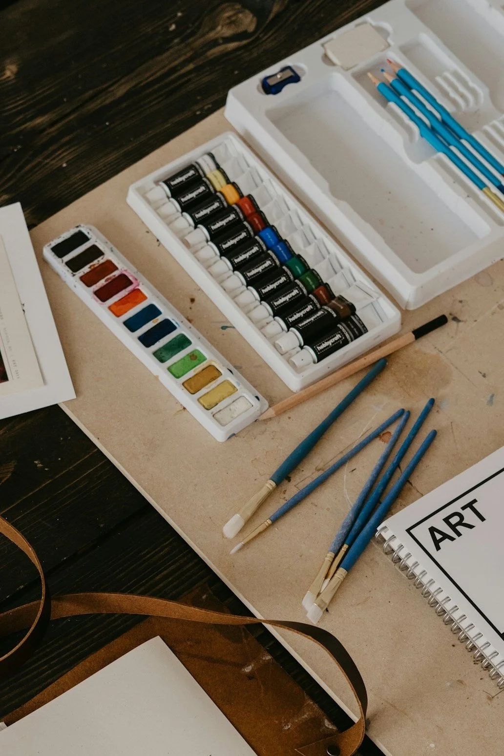 Watercolor paints, brushes, and art supplies on a wooden table.