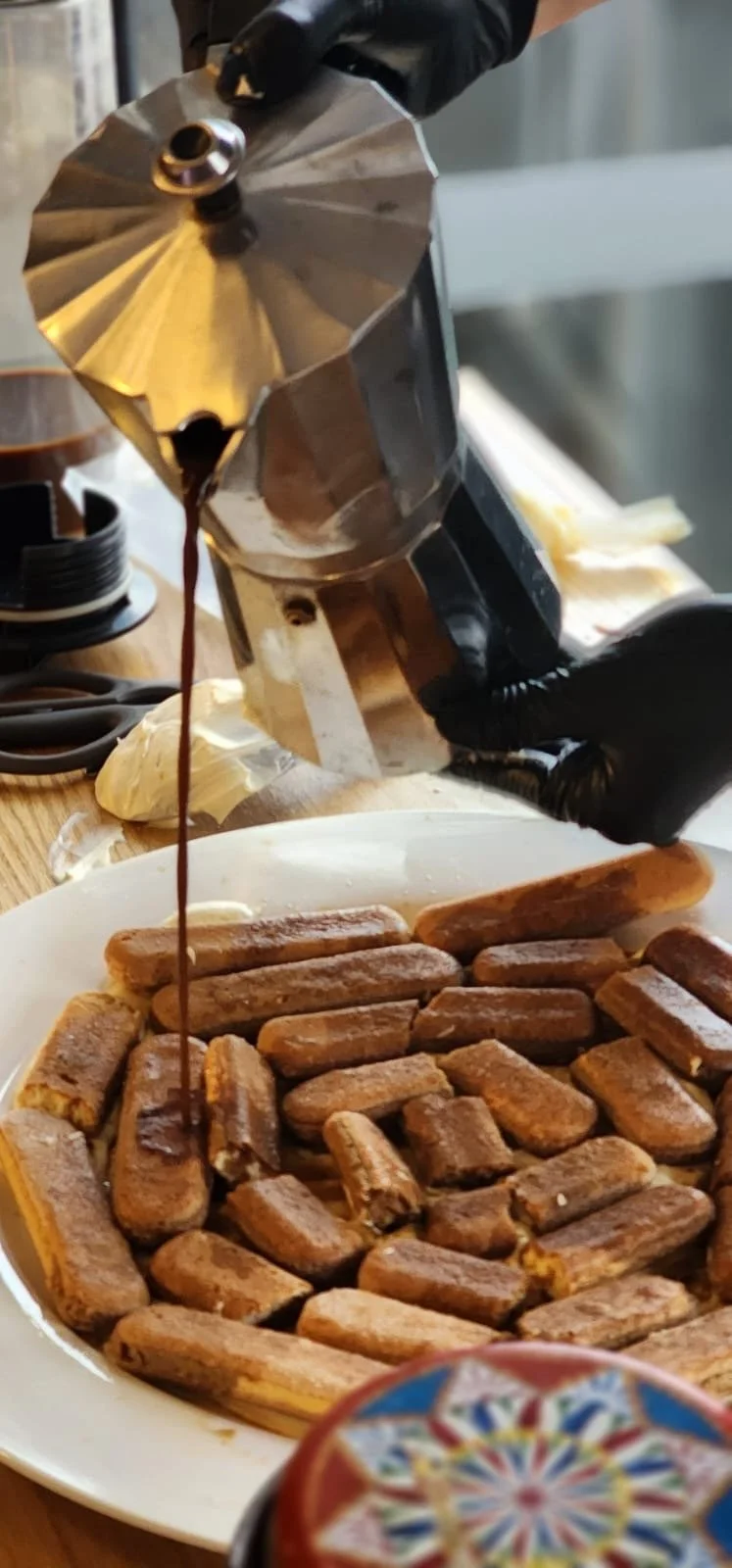 espresso coffee being poured over ladyfinger biscuits for tiramisu preparation