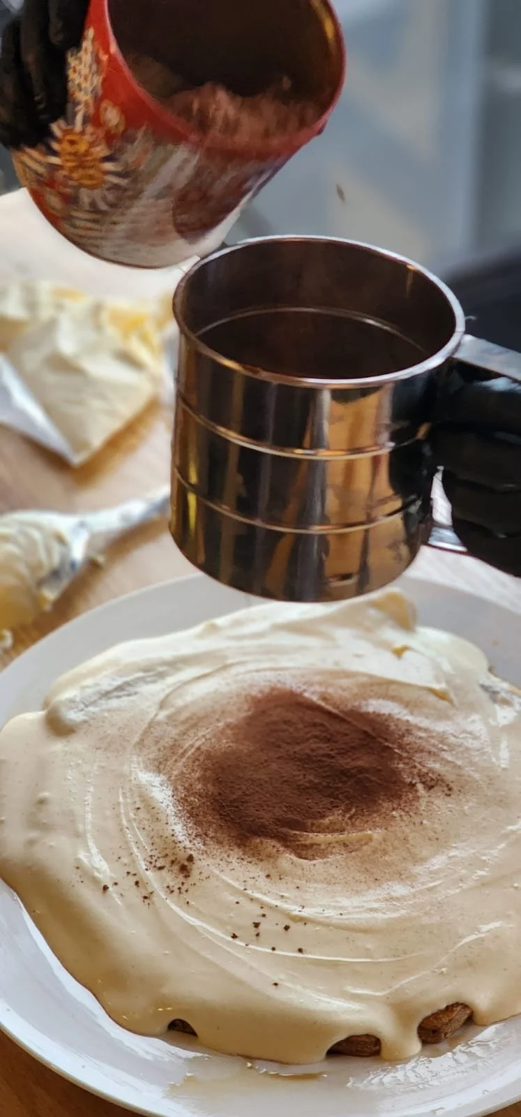 cocoa powder being dusted over fresh tiramisu during live dessert preparation