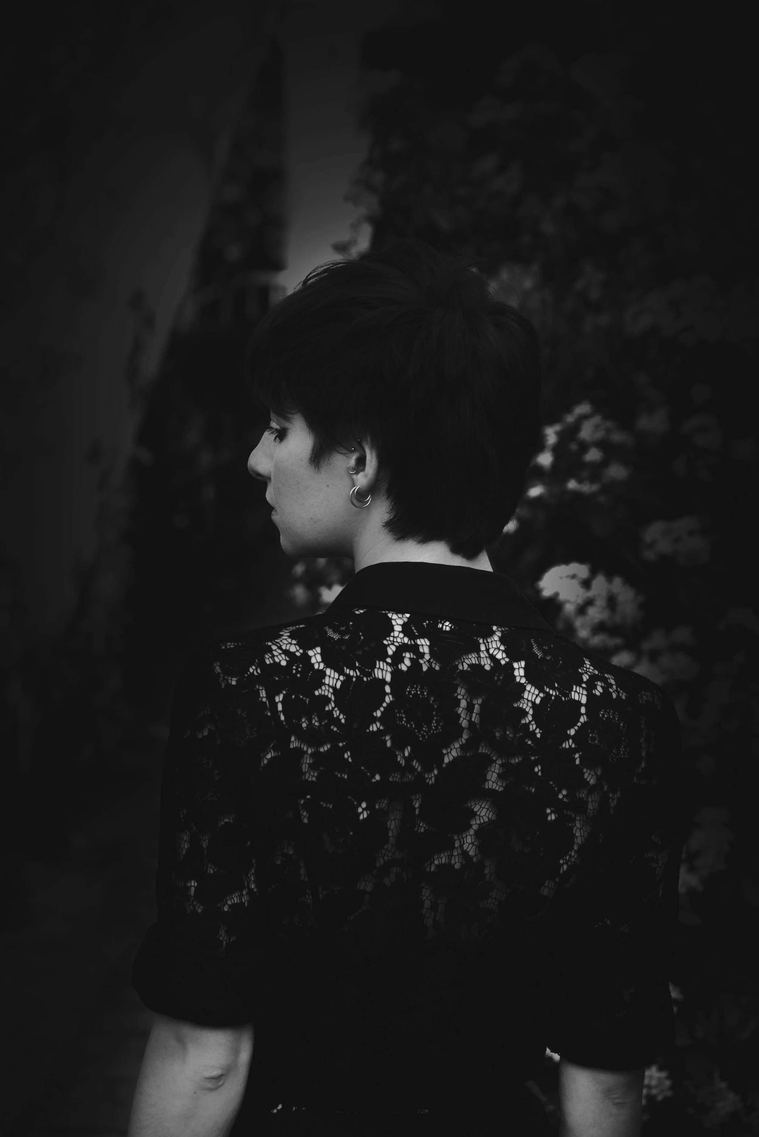 Un portrait en noir et blanc d'un homme avec des cheveux attachés, une barbe fine, portant un t-shirt noir, dans un environnement naturel flou.