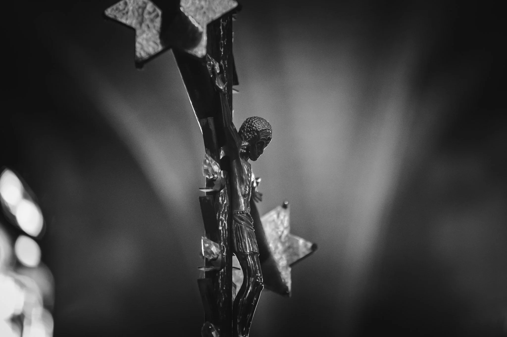 Une croix en bois avec une figure de Jésus crucifié, entourée de lumières floues en arrière-plan, dans une ambiance sombre et solennelle.