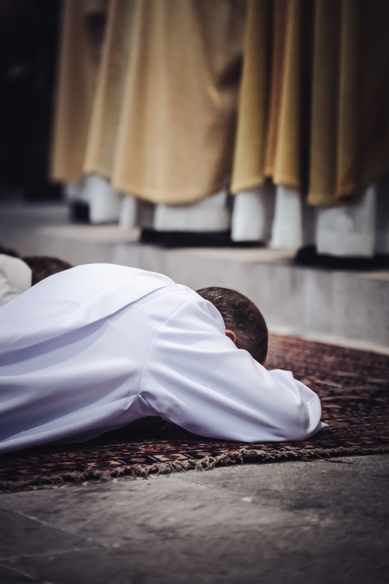 Un futur diacre en vêtement blanc en position de prosternation sur un tapis de prière lors de son ordination.