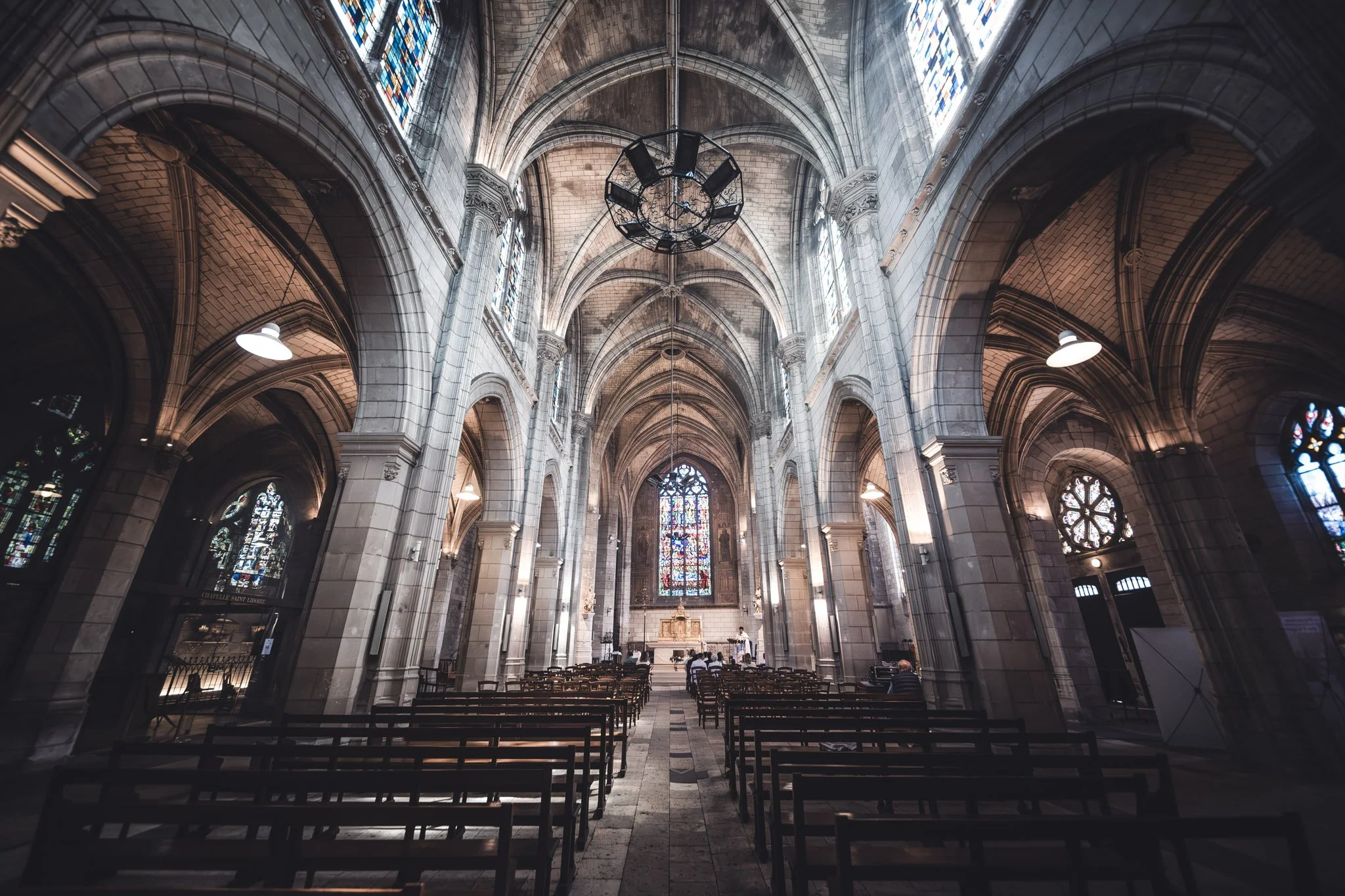 Intérieur d'une vieille église gothique avec des vitraux colorés, arches en pierre, chaises en bois, et un autel au fond.