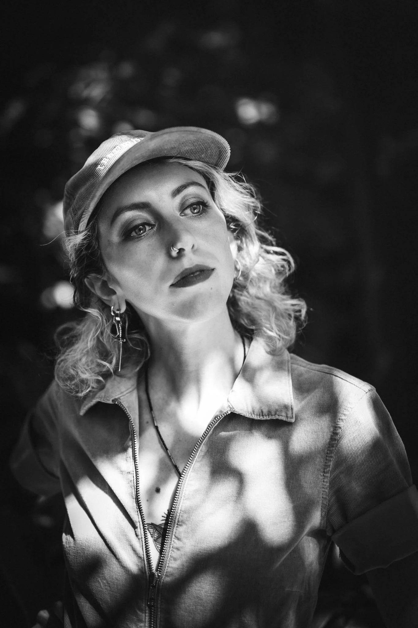 Portrait d'une femme portant une veste en denim, un chapeau et des boucles d'oreilles, en noir et blanc.