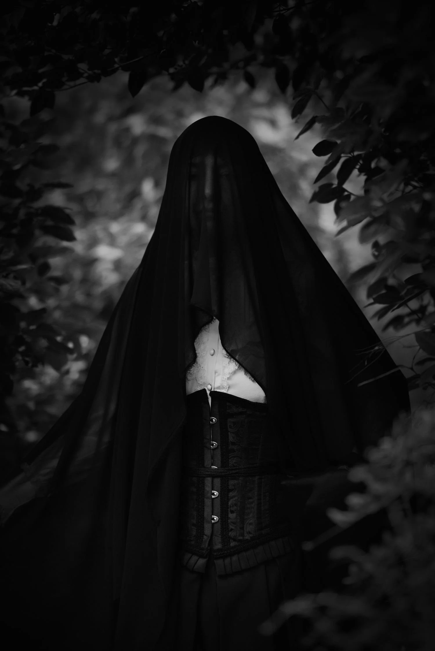 Figure féminine vêtue d'une robe blanche et d'un corset noir, portant un voile noir qui couvre son visage, dans un environnement sombre et mystérieux entouré de feuilles.