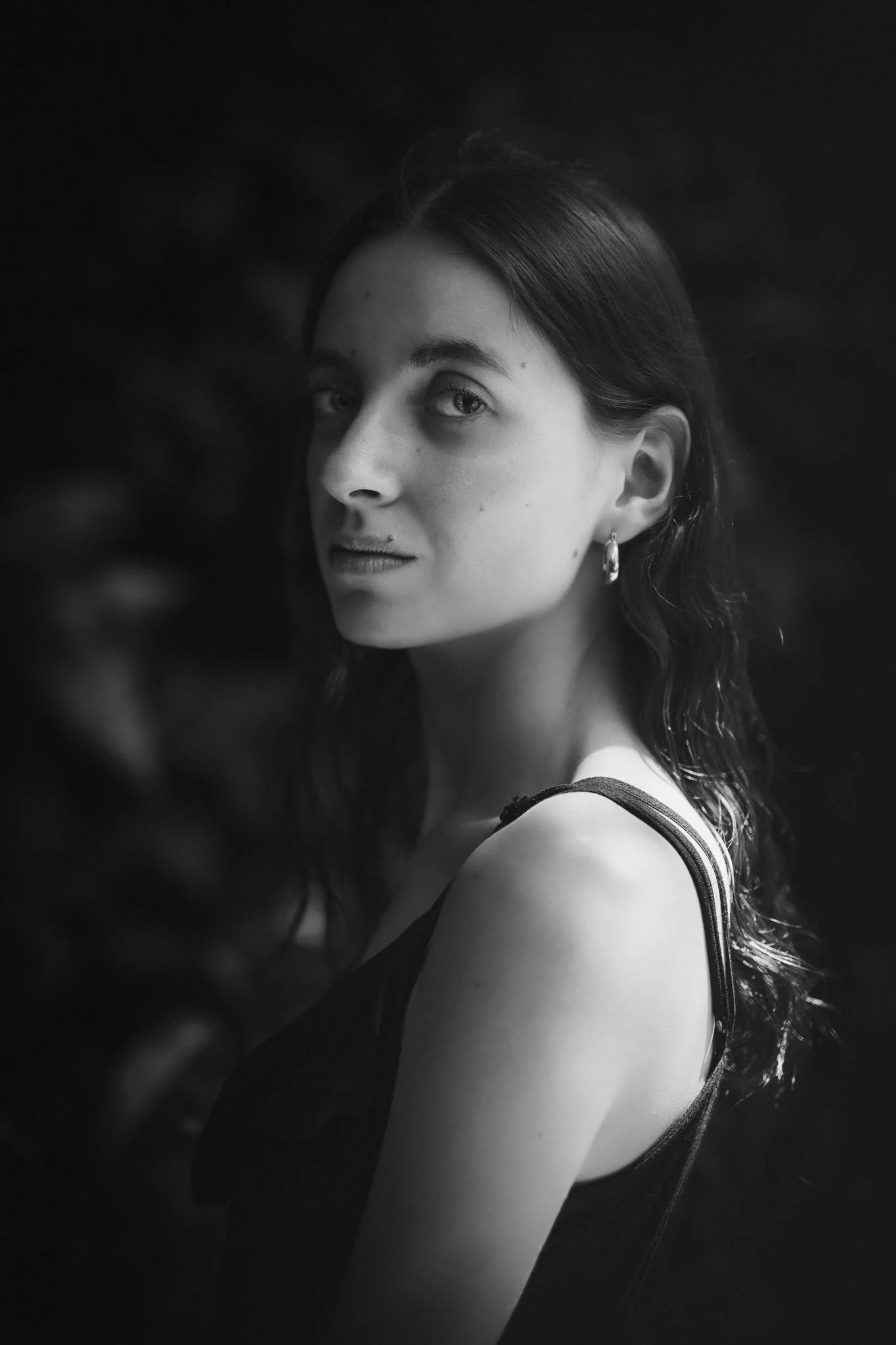 Portrait en noir et blanc d'une jeune femme regardant vers l'objectif, portant une robe sans manches, avec des boucles d'oreilles.