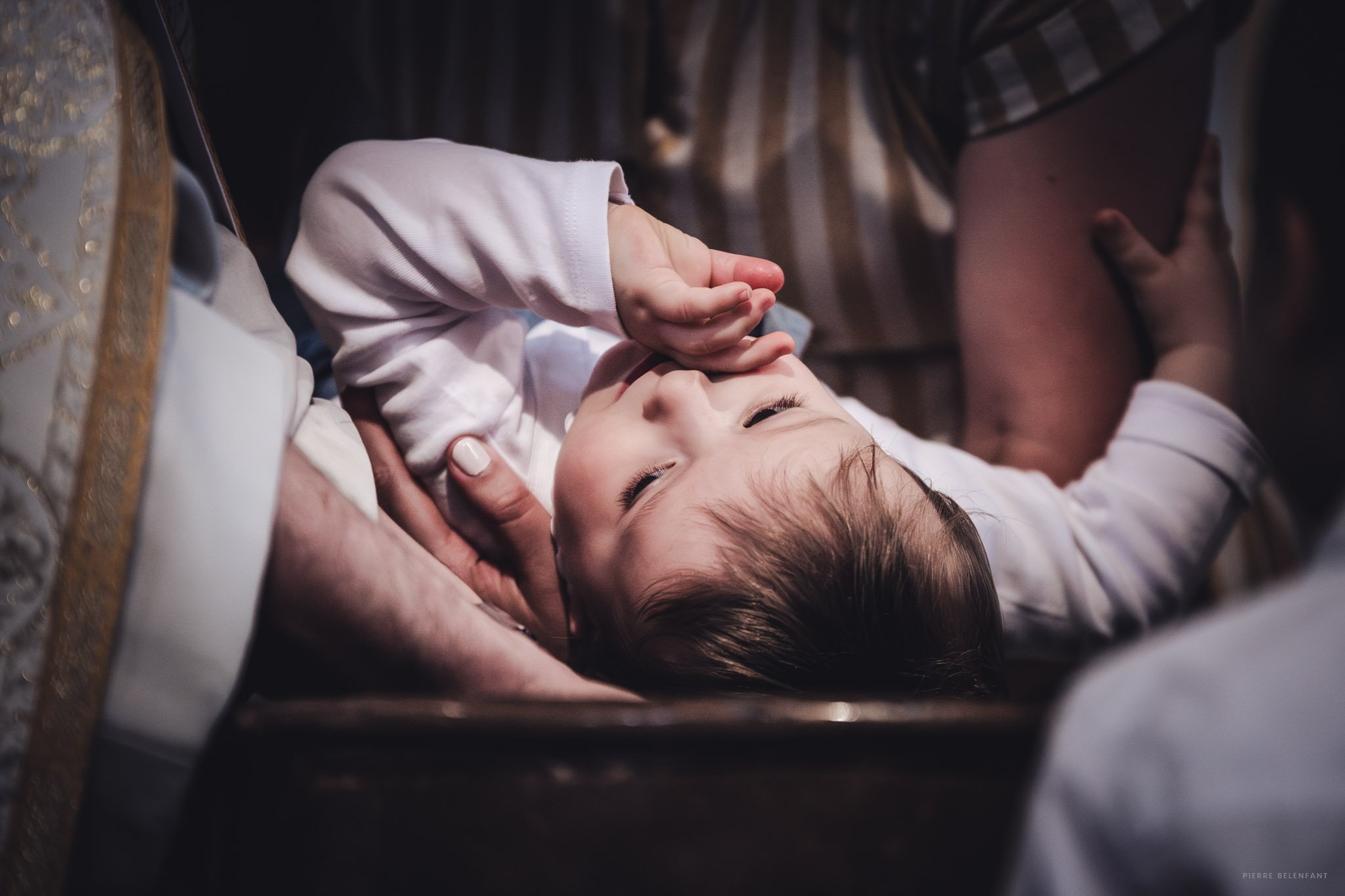 Un bébé avec un prêtre tenant sa tête, lors du baptême.