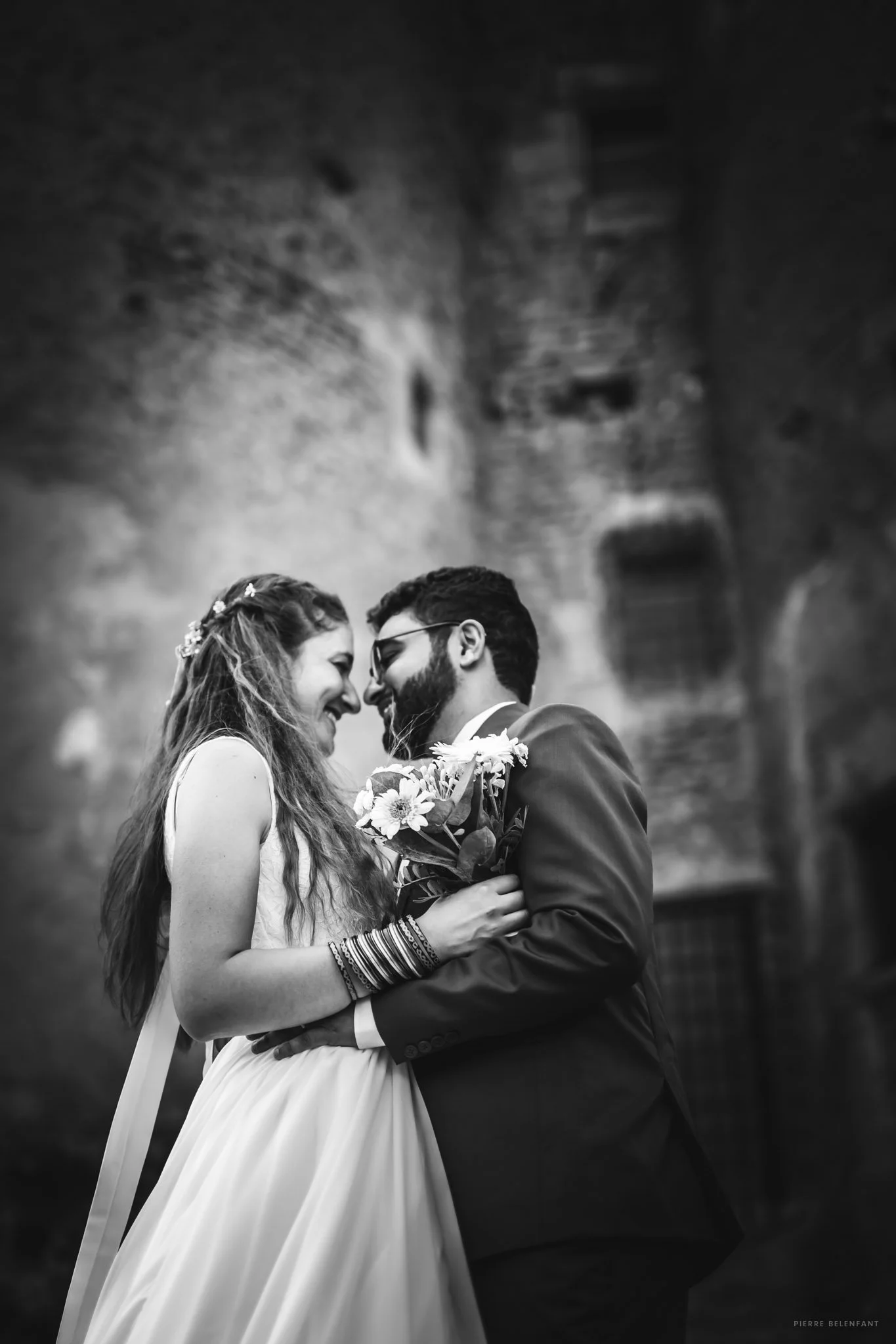 Deux personnes en mariage, un homme et une femme, se regardant tendrement avec un sourire, dans une ambiance romantique, en noir et blanc.