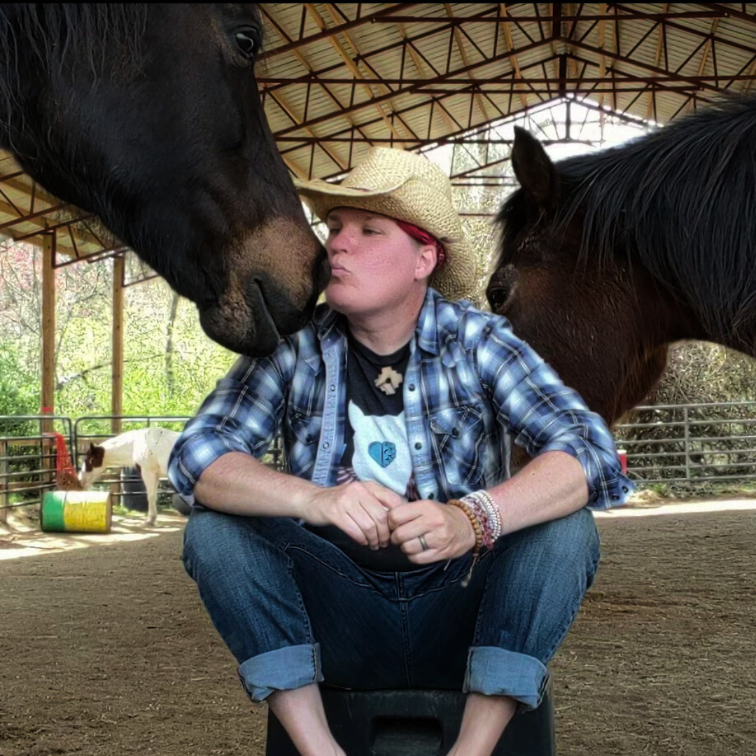 Picture of Kel Hansen in a cowboy hat sitting among horses, and kissing one on the nose.