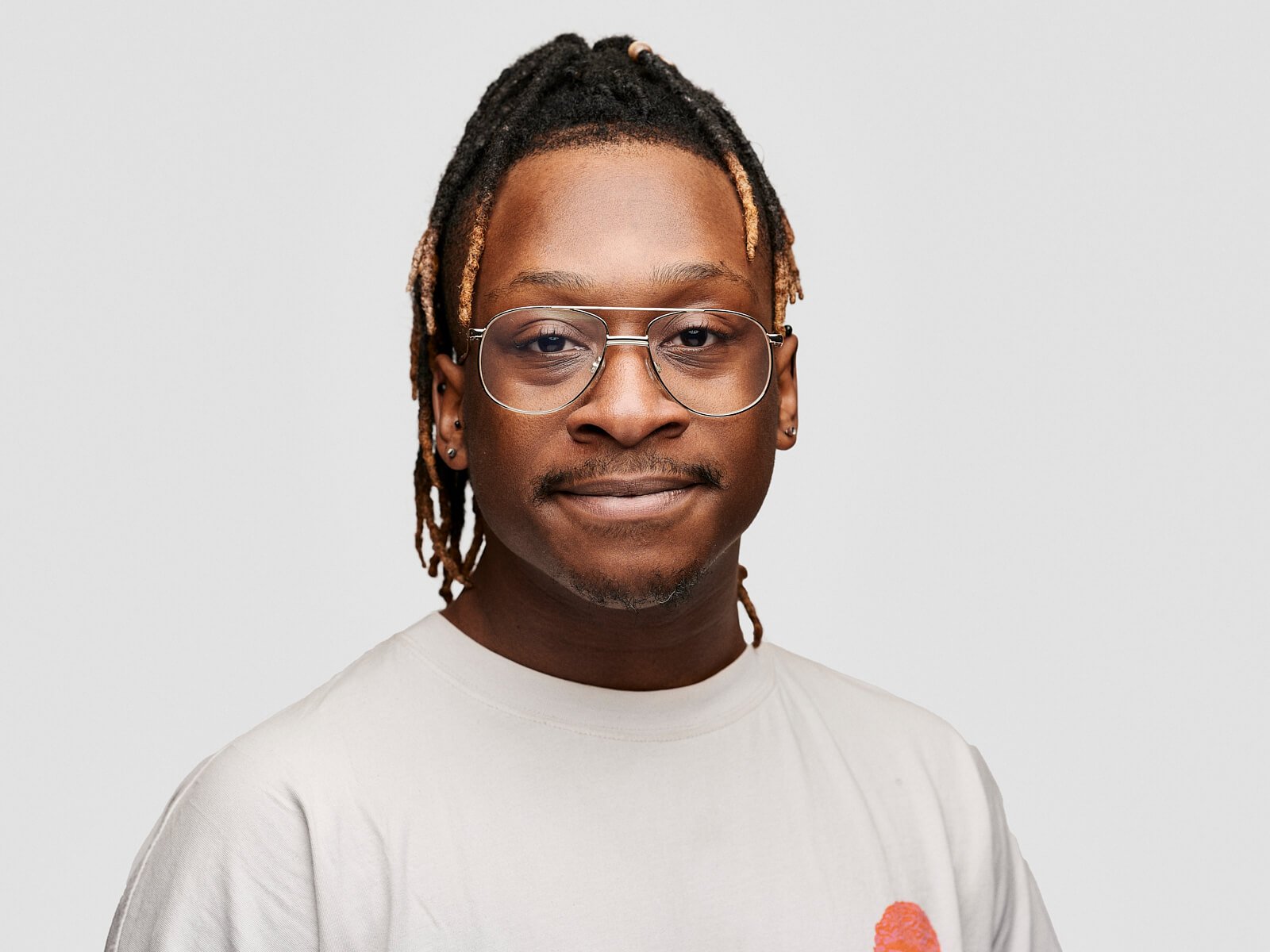 Team headshot of smiling black man with dreadlocks and glasses against a white background