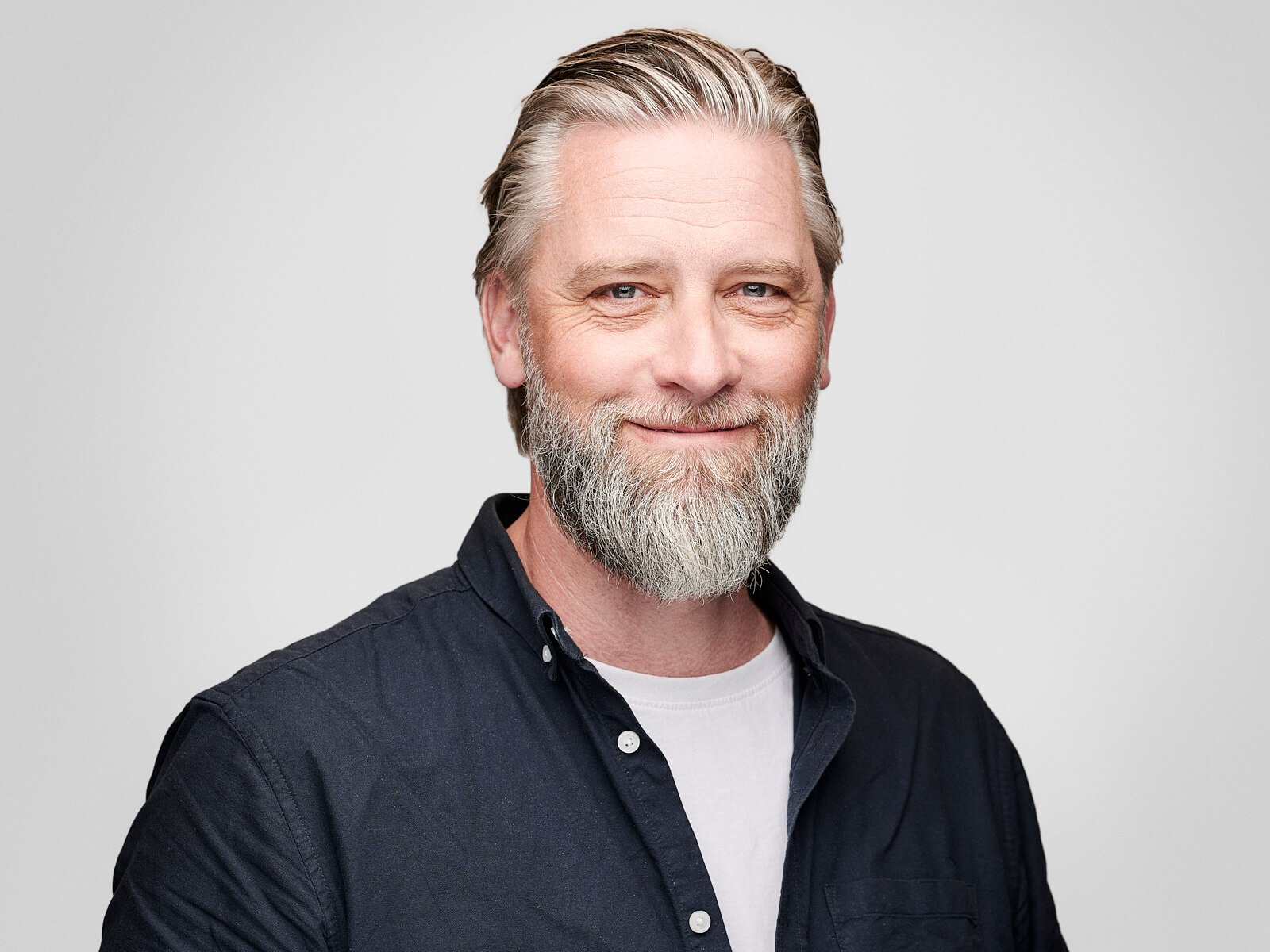 Team headshot of smiling man with grey beard and black shirt against a white background