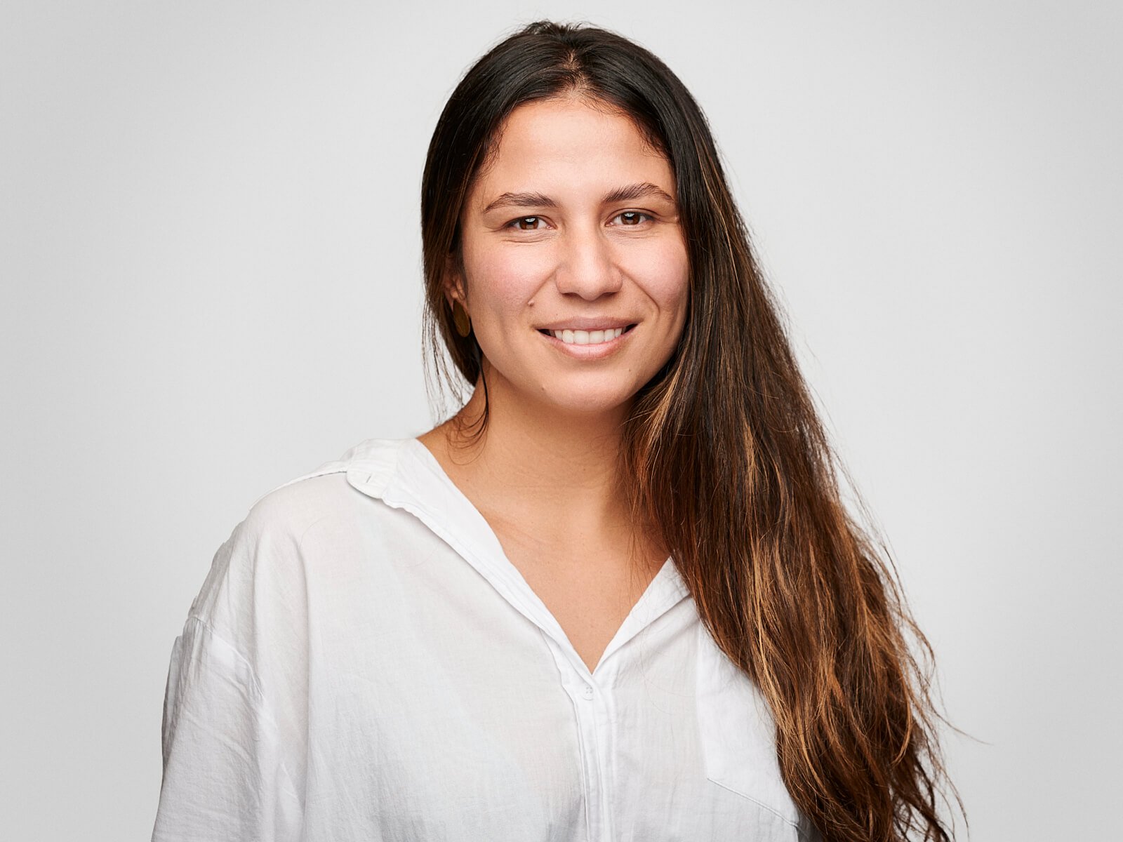 Team headshot of simling woman with long dark hair and a white shirt
