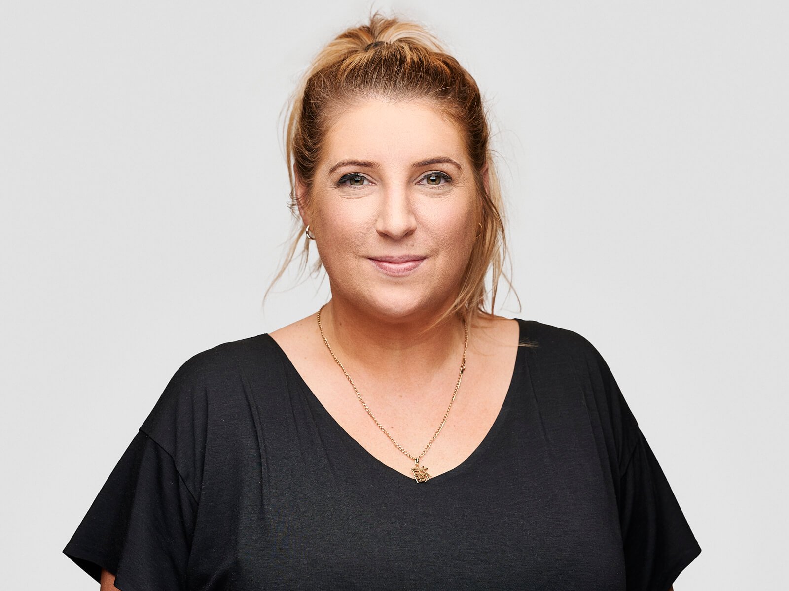 Business team headshot of smiling woman with tied back hair wearing a black t-shirt against a white background