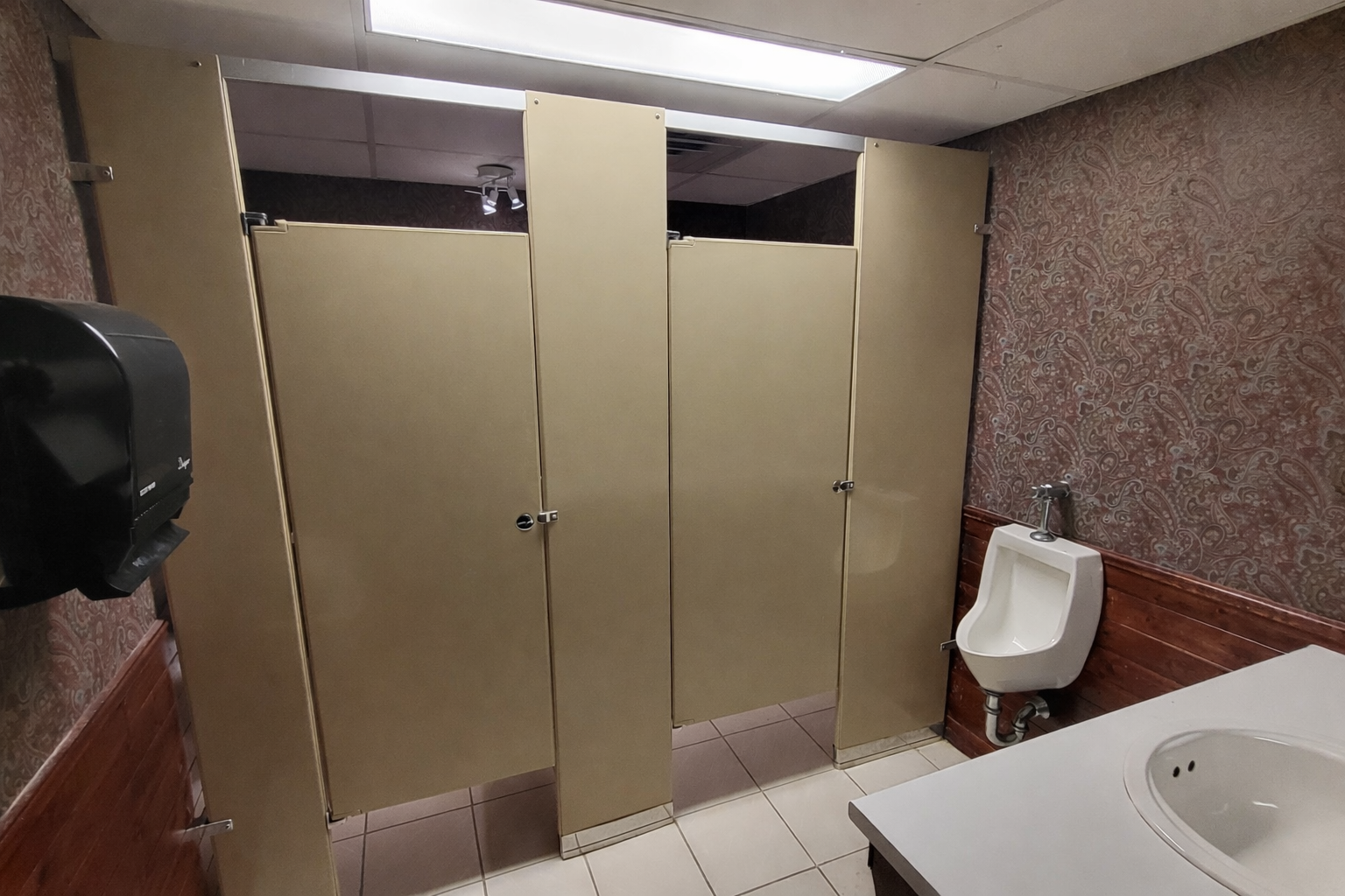 Men's restroom with beige partitions and fixtures.png