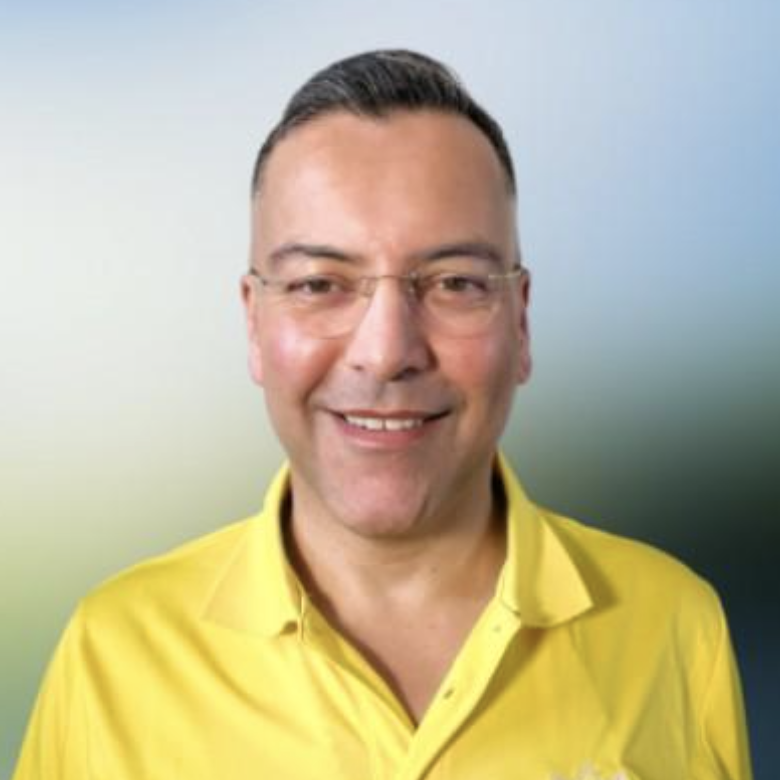 Smiling man wearing glasses and a yellow shirt, with a blurred blue and green background.