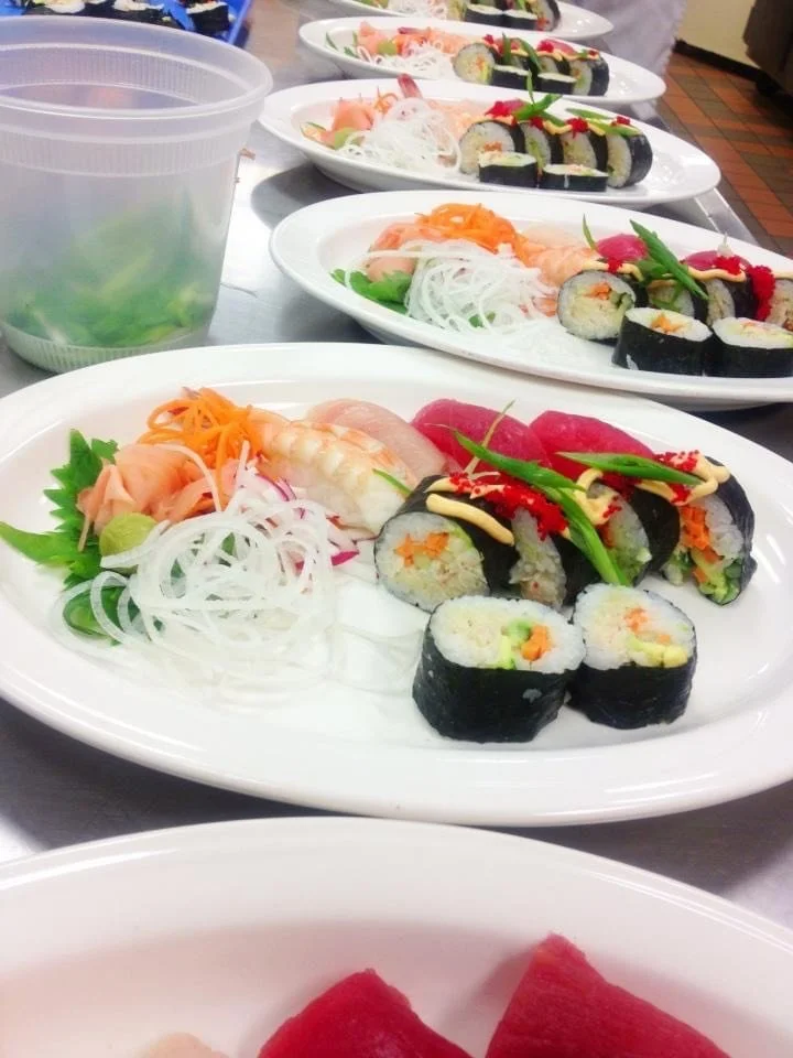 Multiple plates of sushi featuring various rolls, sashimi, and garnishes with vegetables and sauces on a table.