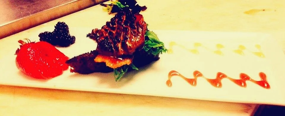 Gourmet burger slider with lettuce, a dollop of sauce, and a side of berries on a white rectangular plate.