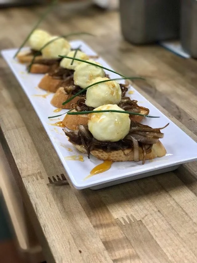 Several pieces of bread topped with shredded meat, cheese, and dollops of mashed potatoes, garnished with chives, served on a rectangular white platter.