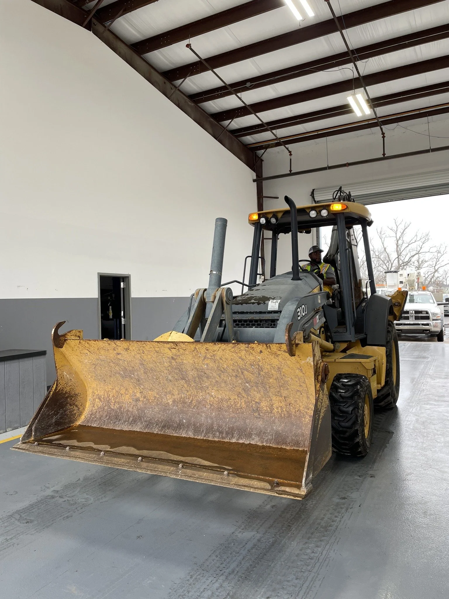 Yellow and gray bulldozer inside a garage, with a person wearing a helmet and reflective vest operating it.