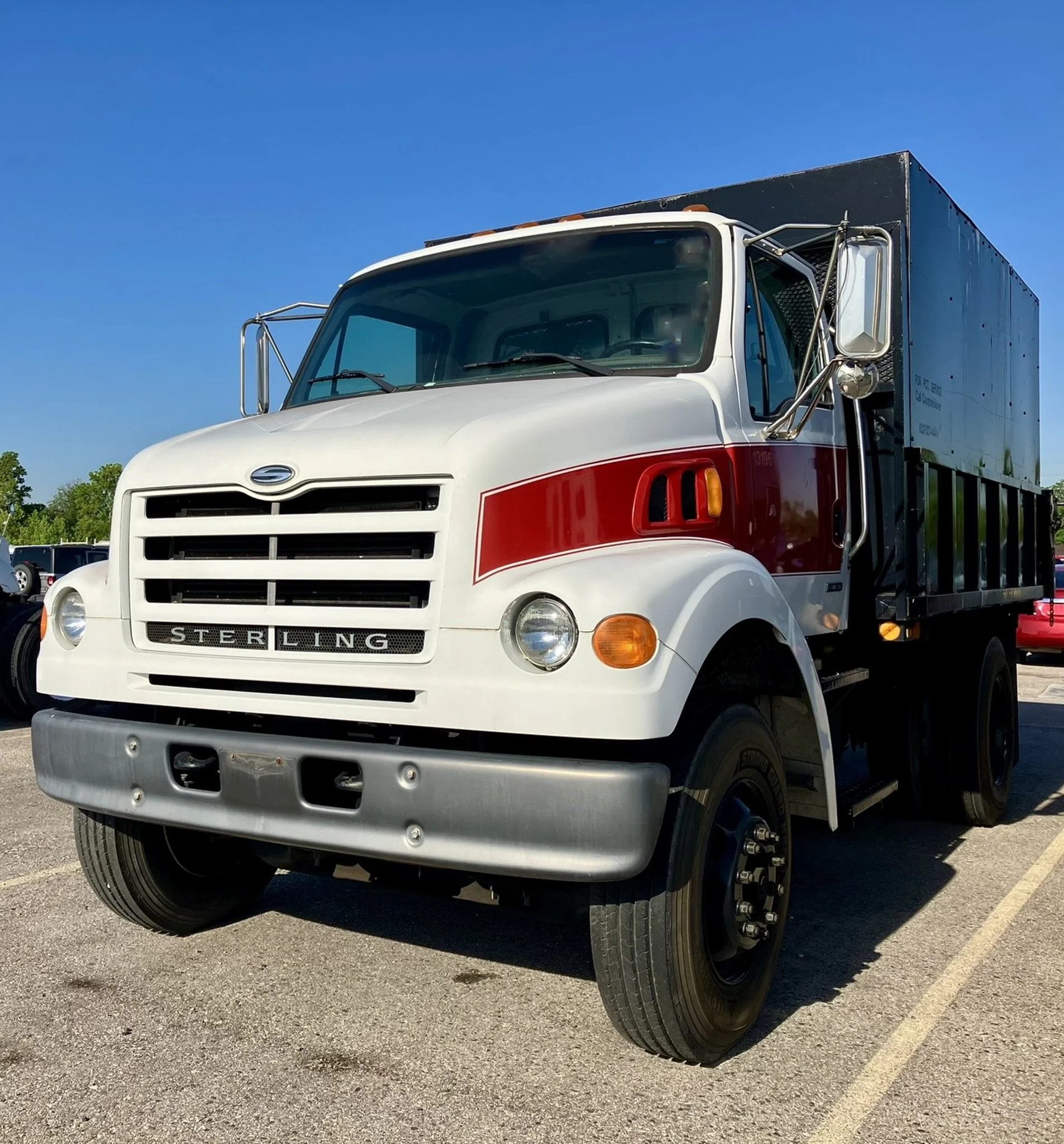 A vintage Sterling truck with a white cab, red stripe, and a black cargo bed, parked outdoors under a clear blue sky.