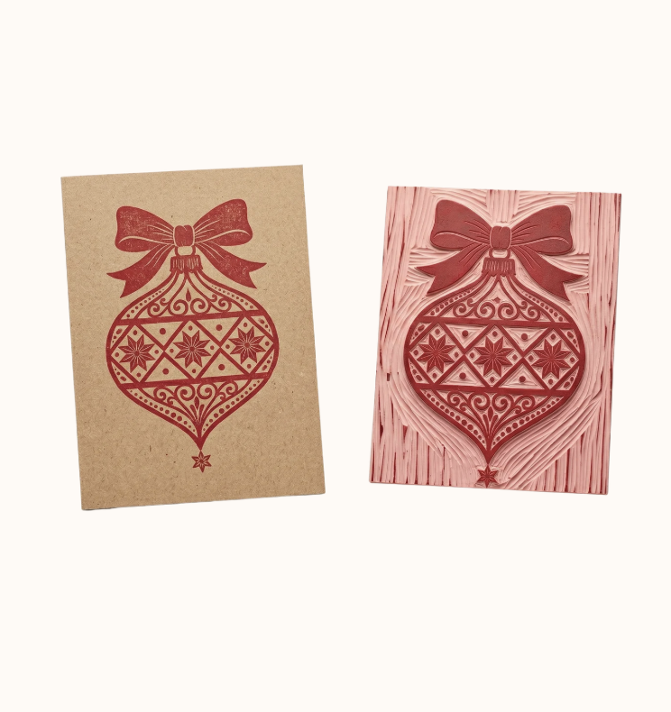 A rubber stamp and a card with a Christmas ornament design, featuring a bow and intricate patterns.