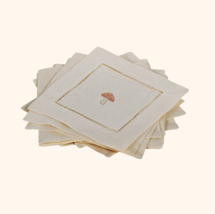 Stack of beige cloth napkins with embroidered mushroom design in the center