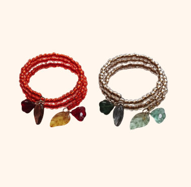 Two beaded bracelets with charms, one red with a black charm and yellow stone, the other silver with black and green charms and green and clear stones.