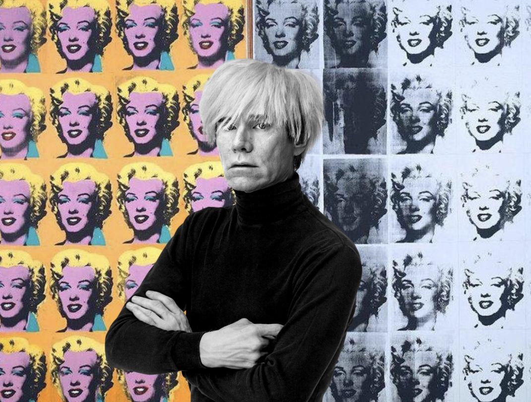 Three men are in a room decorated with large colorful flower cutouts on the walls and on the ground. One man sitting on a white chair in the foreground, wearing sunglasses and a blue jacket, is resting his head on his hand. The other two men are standing in the background, one with his arms raised and the other holding a camera or a phone. The floor has rugs with flower patterns, and the overall scene appears to be a stage or an art installation.