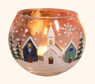 Decorative glass bowl with a snowy village scene featuring a church, houses, pine trees, snowflakes, and a lit candle inside.
