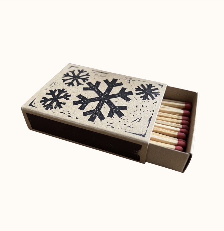 A cardboard box of matches with a snowflake design on the cover, partially opened to reveal wooden matches inside.