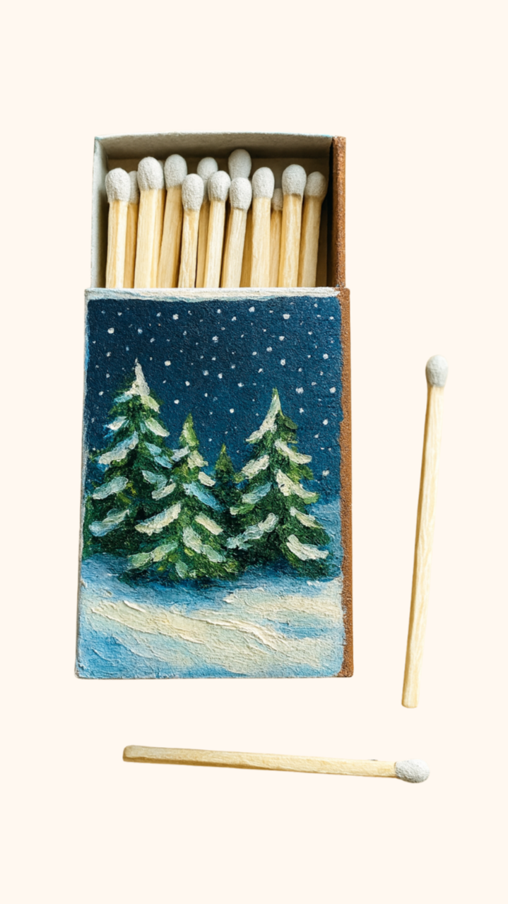 A matchbox with a painted winter scene of pine trees and snow, some matches removed from the box and others inside, on a light background.