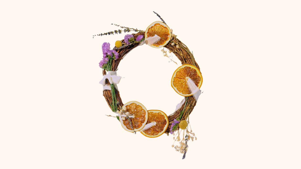 A letter Q made from a wreath of twigs decorated with dried orange slices, purple flowers, and white ribbons.