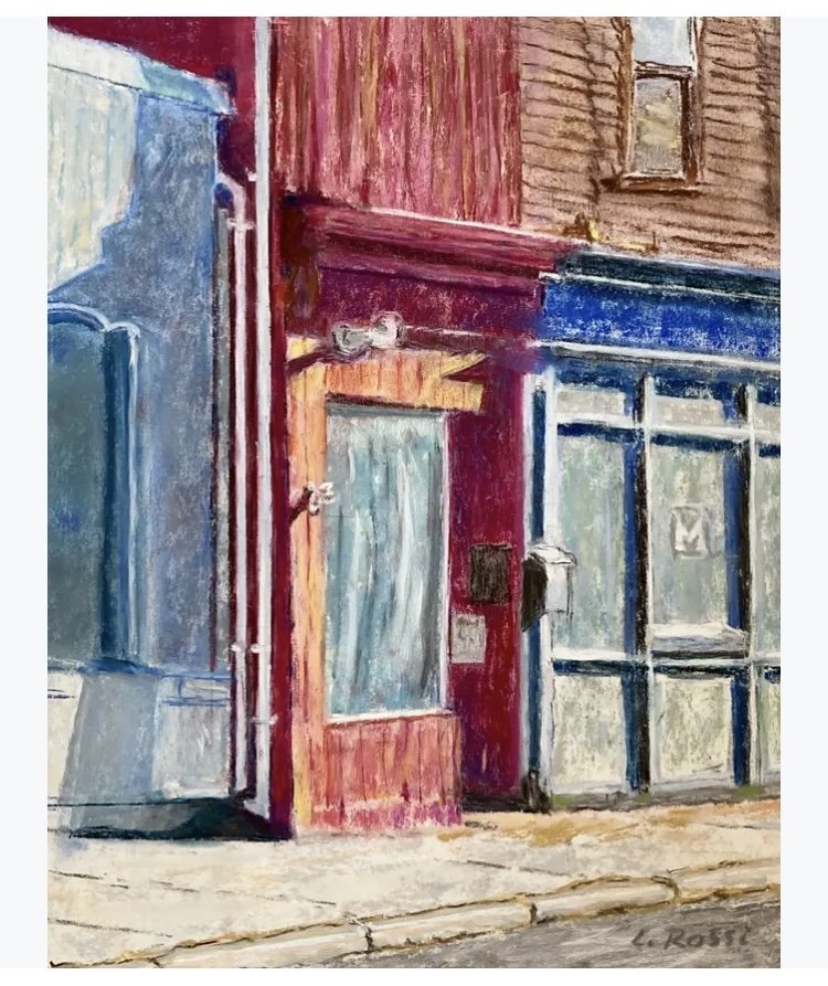 Colorful street corner with store-fronts painted in shades of blue, red, and wood tones, showcasing windows, door, and sidewalk.