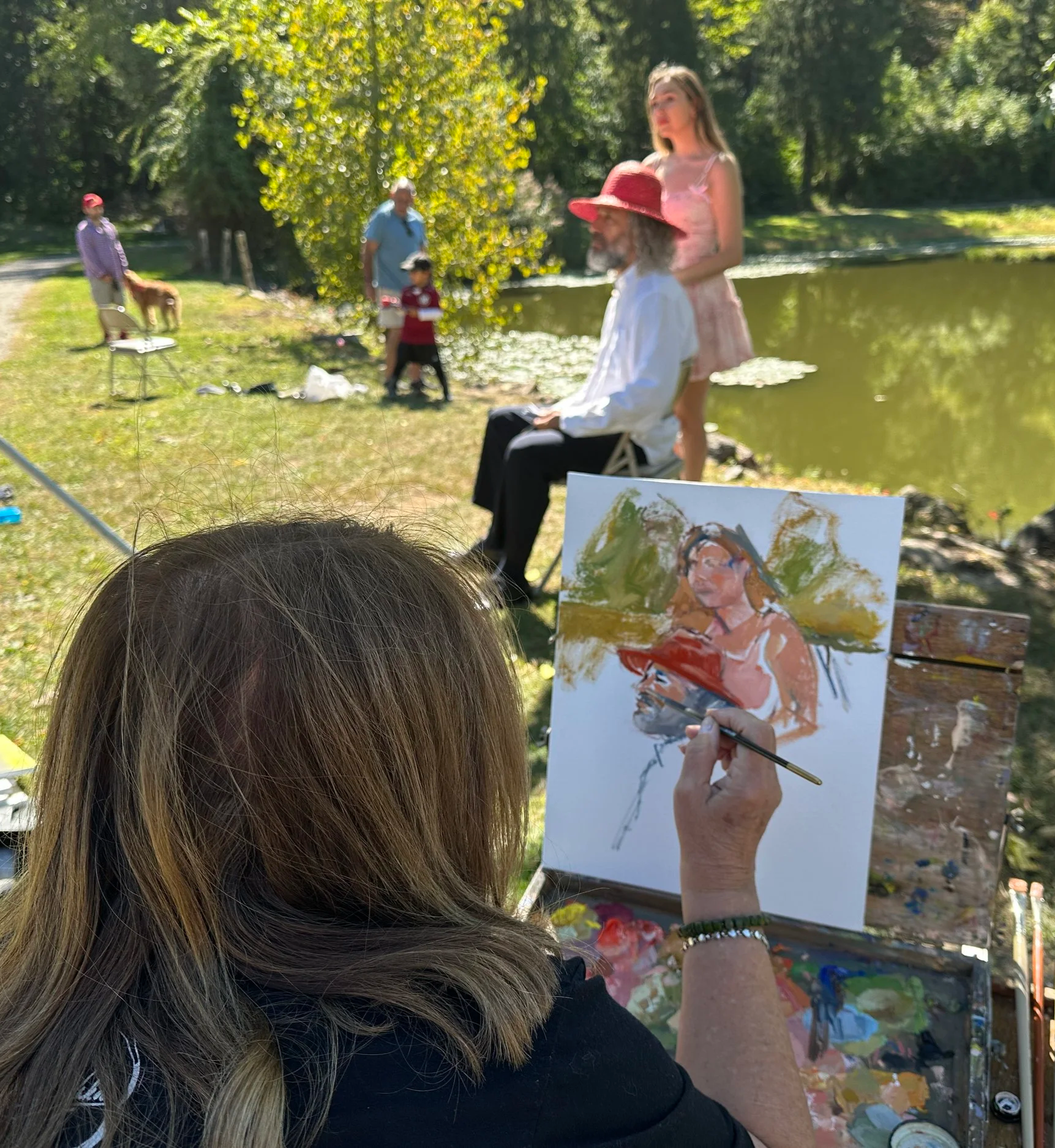 Artist painting two posed people outside by a pond