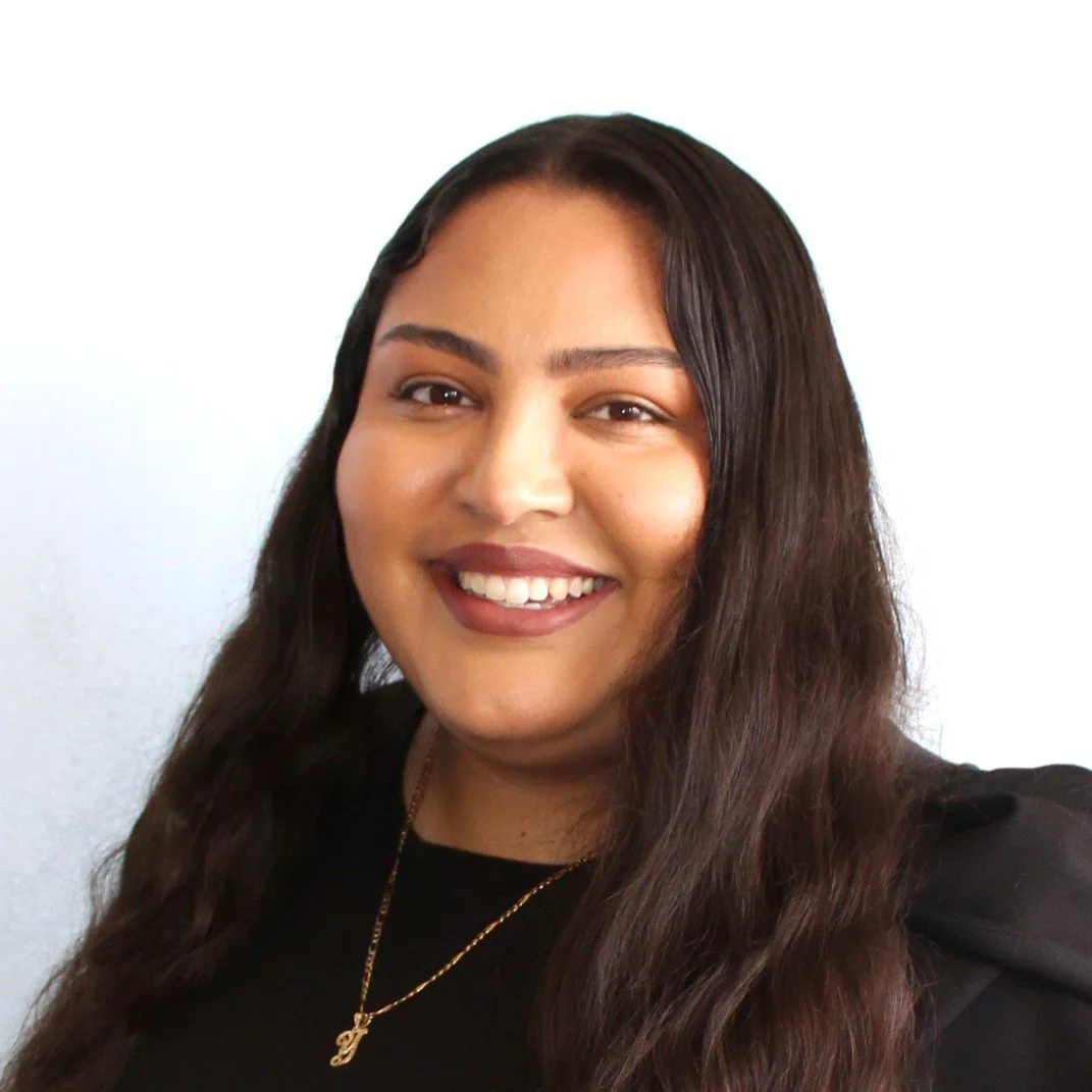 Smiling woman with long dark brown hair wearing a black blouse and gold necklace.
