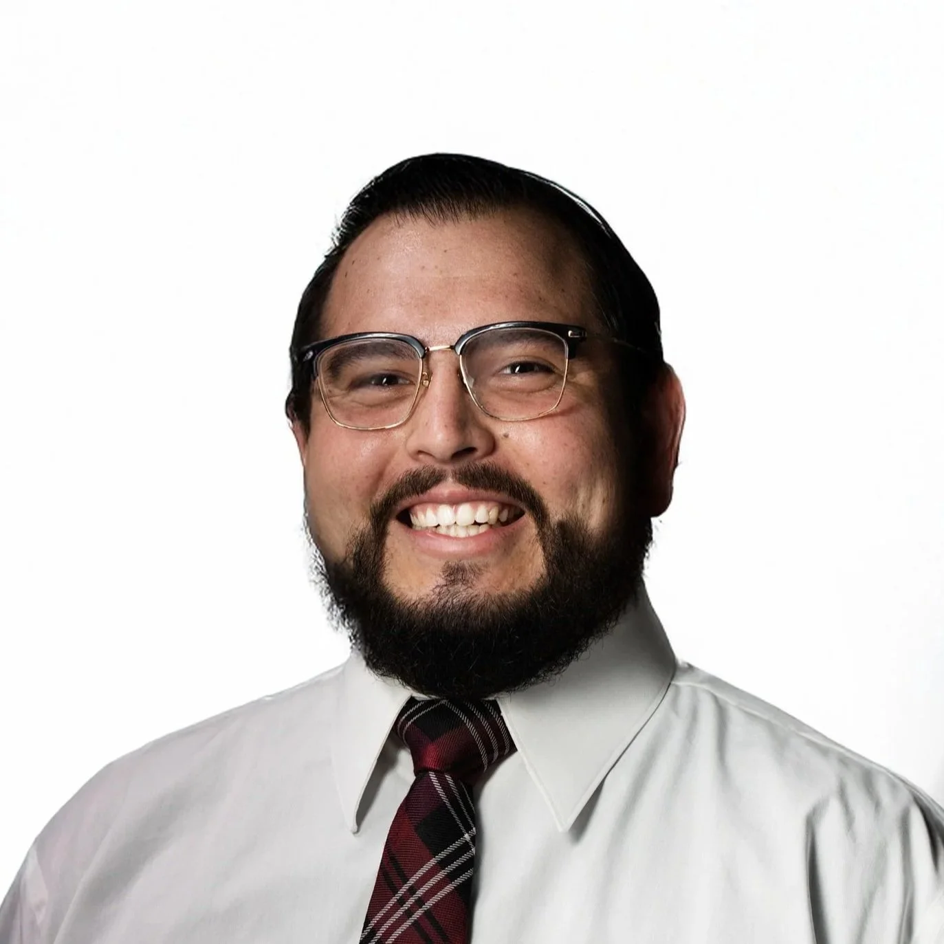 Smiling man with short black hair, full beard, wearing glasses, a white collared button up shirt, and red plaid tie.