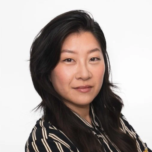 Smiling woman with long dark brown hair wearing a black and white striped collared shirt.