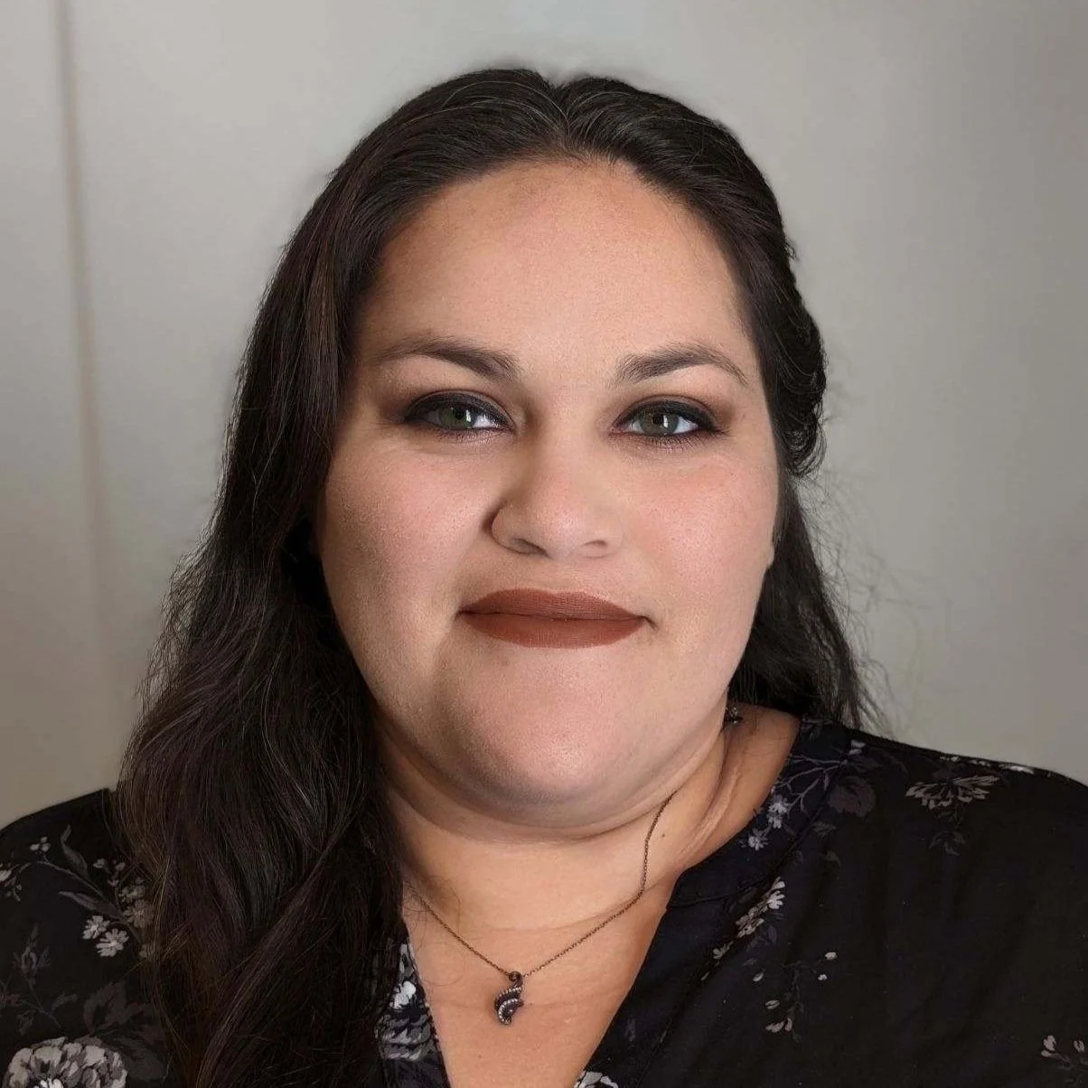 A woman wearing dark lipstick wearing a dark floral top with a small necklace.