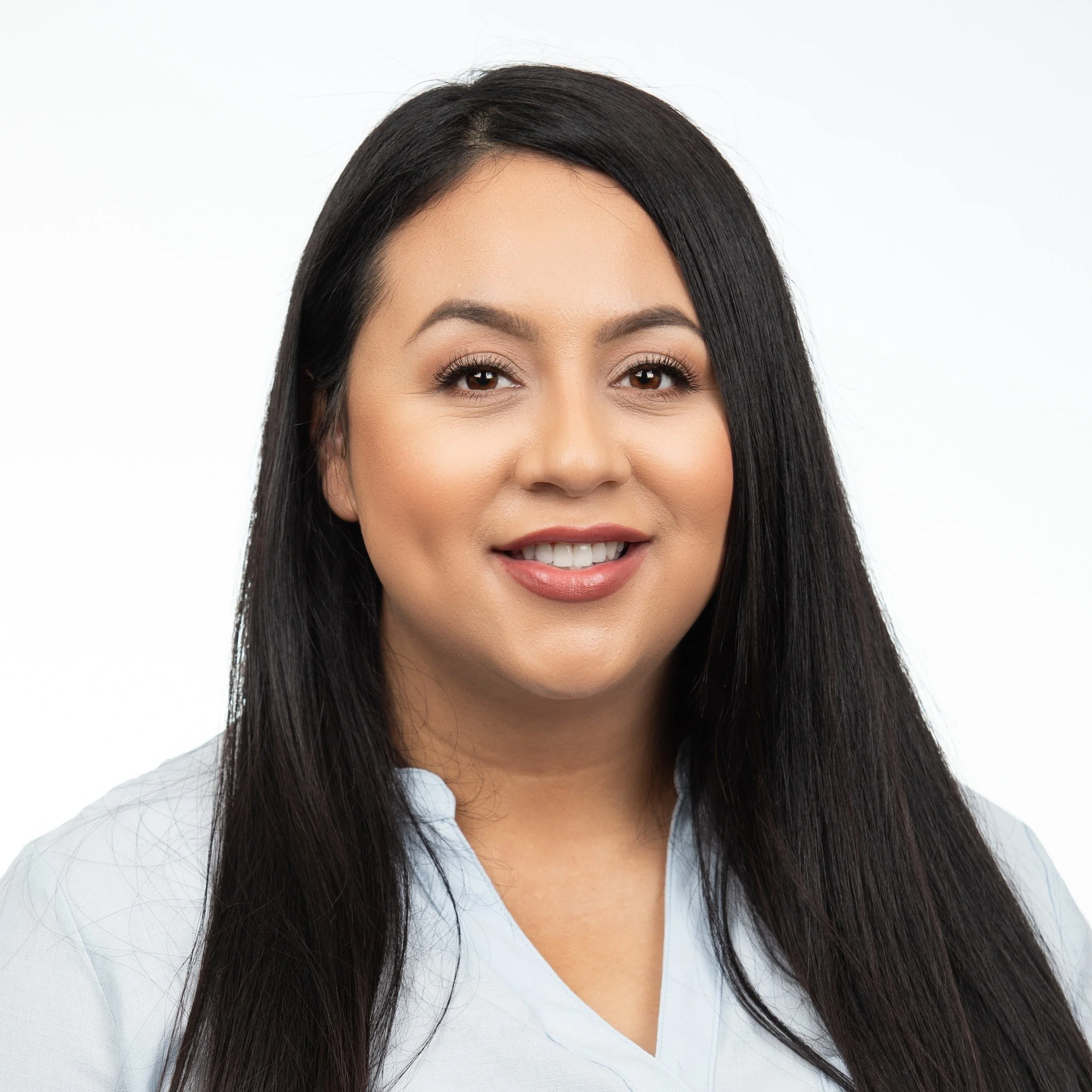A woman smiling with long dark hair wearing a light blue blouse.