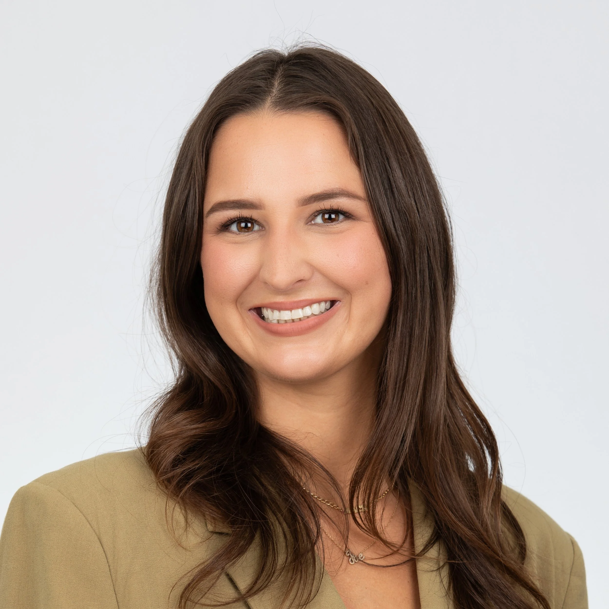 A smiling woman with long brown hair wearing a olive green top.