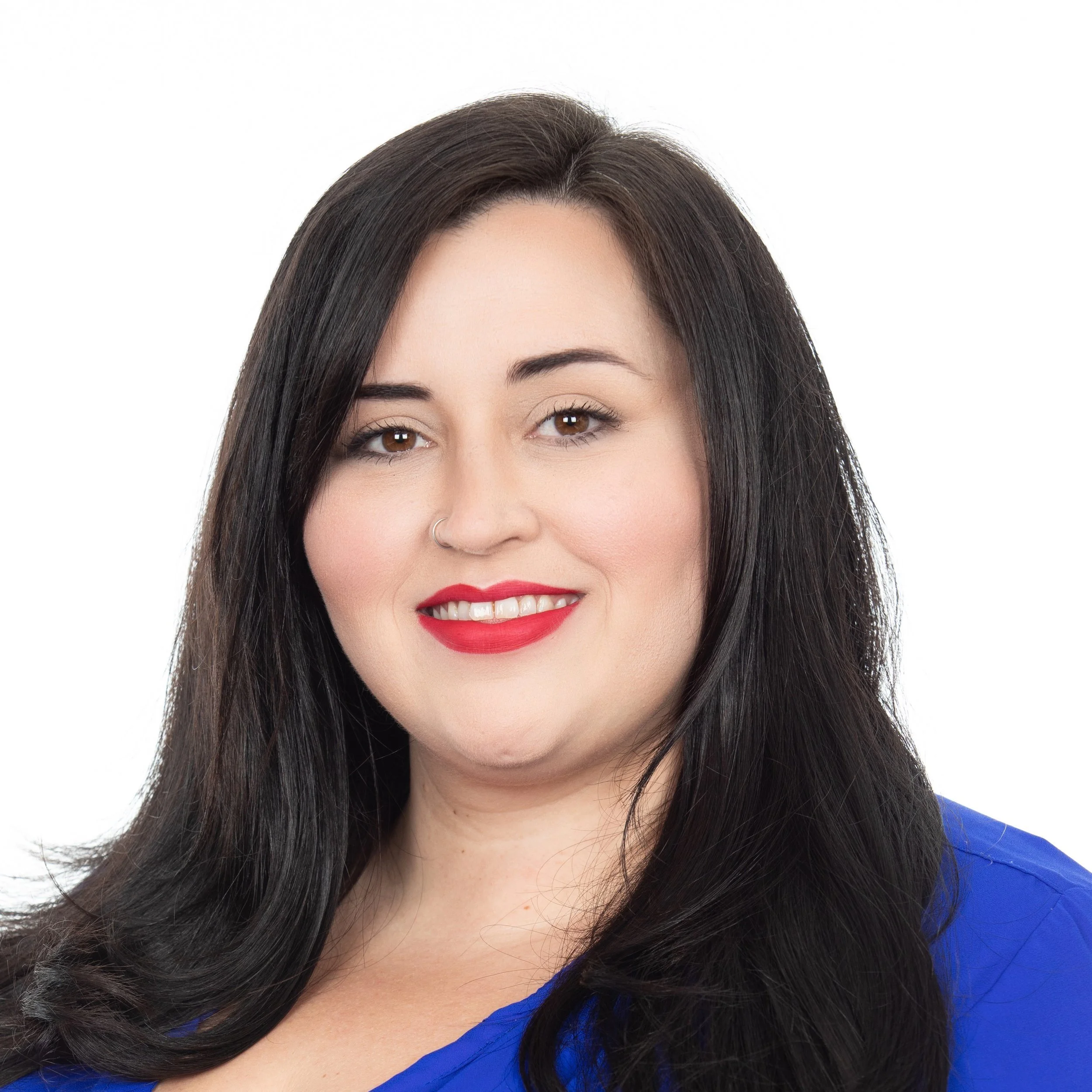A woman smiling with long dark hair with red lip stick wearing a blue top.