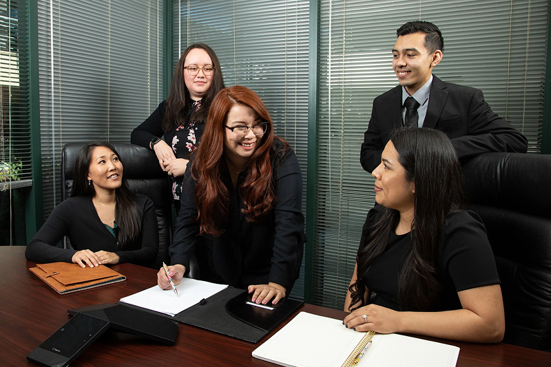 Four woman and a man dressed in business attire converse in a conference room.