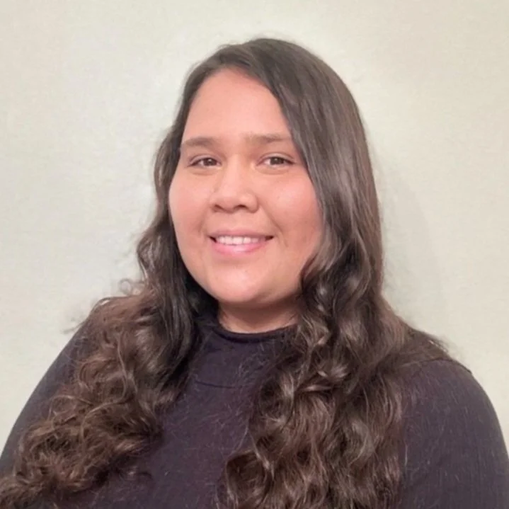 A woman smiling with long curly hair with a dark purple top on.