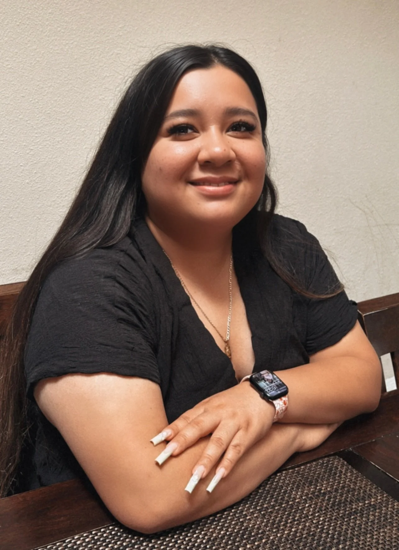 Smiling woman with long dark brown hair wearing a gold necklace and black v-neck blouse.