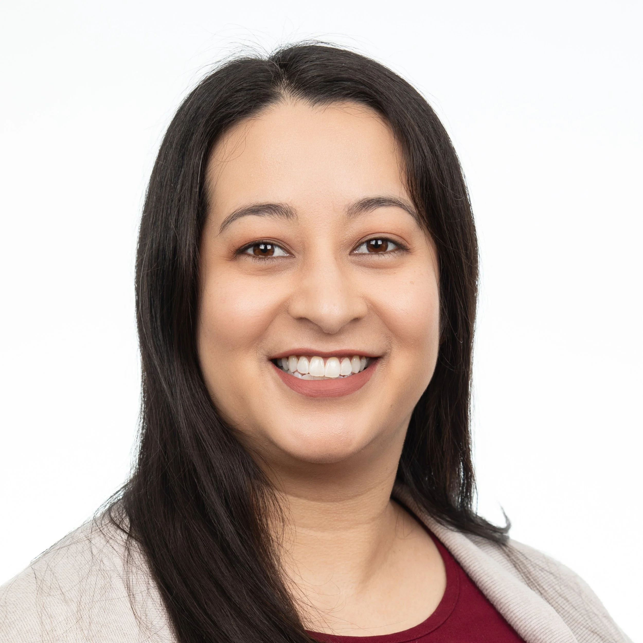A woman smiling with shoulder length brown hair wearing a red shirt with a beige blazer over it.