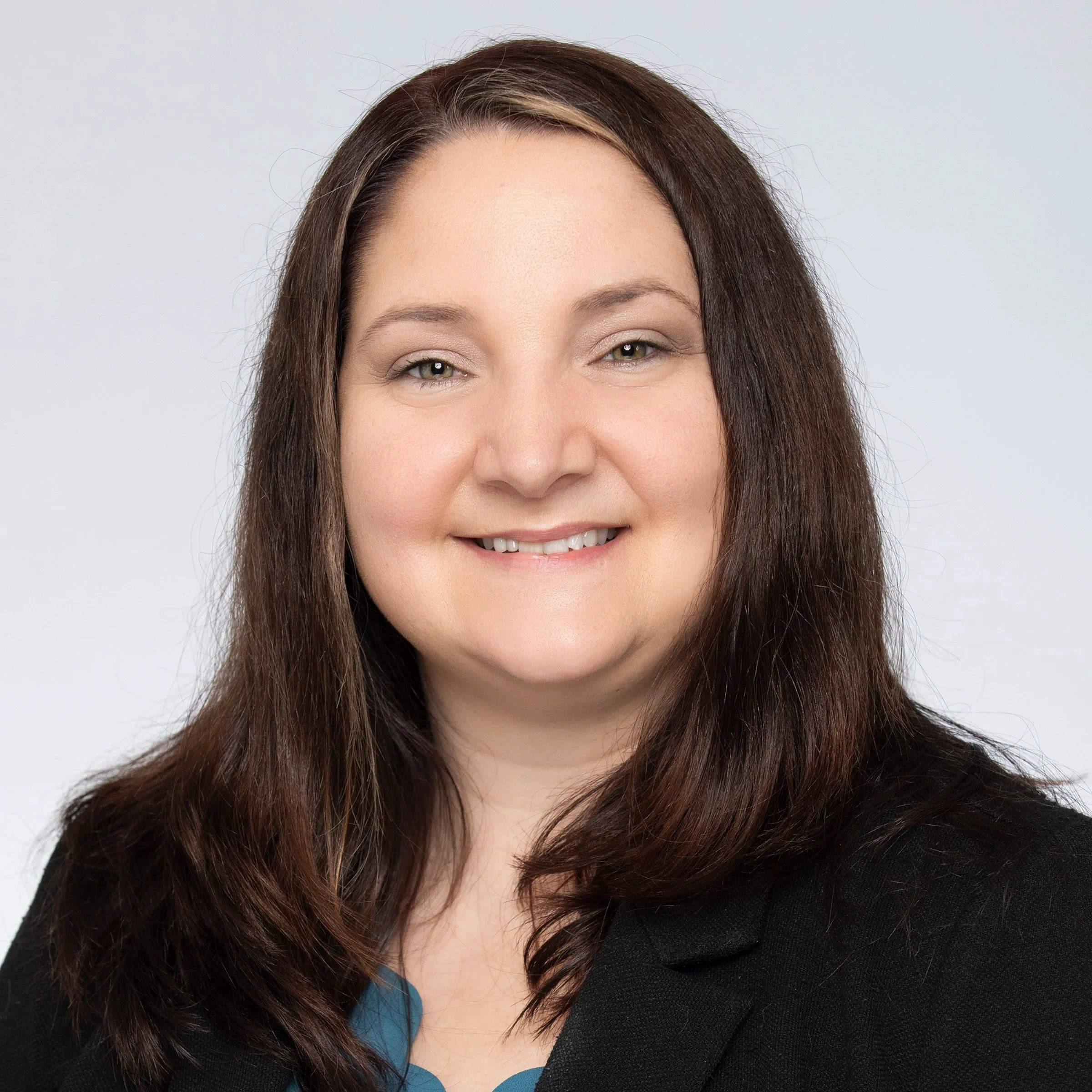 A woman smiling with shoulder length brown hair wearing a blue top and a black blazer over it.
